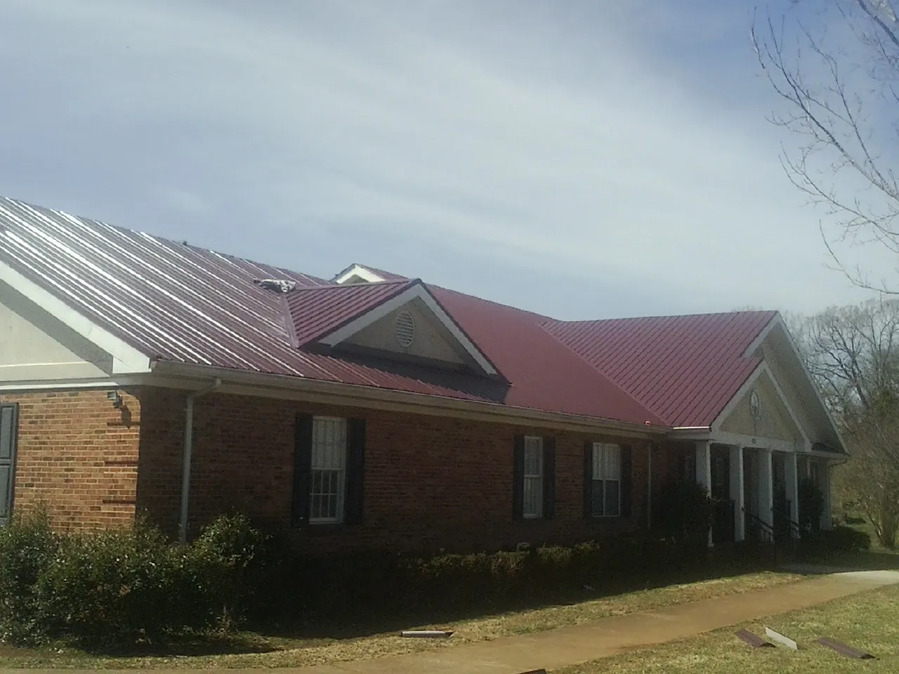 Red metal roof with gabled entries on a long brick building, from a Hail Damage Roof Repair job in Kittanning