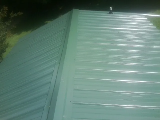 New green metal panels meeting at the ridge of a roof — Flat Roof Repair work by our crew in Kittanning