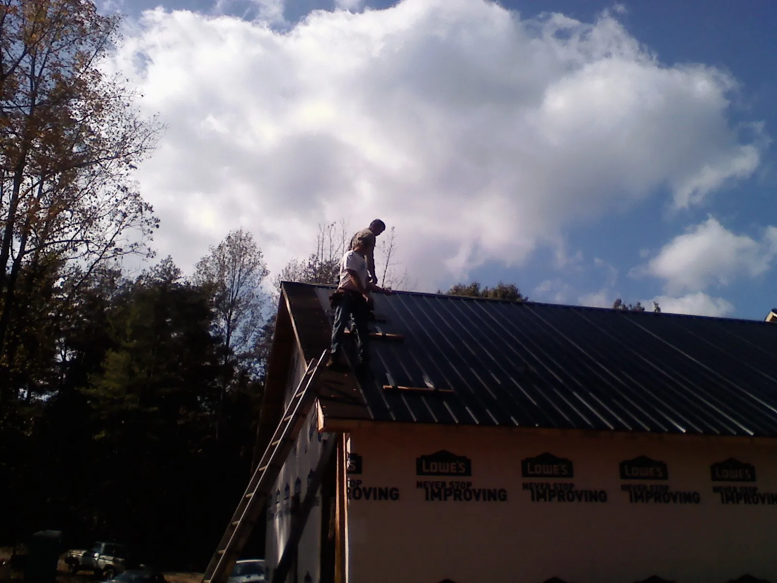 Roofer fastening dark metal panels high against a cloudy sky, from a Roof Inspection job in Kittanning