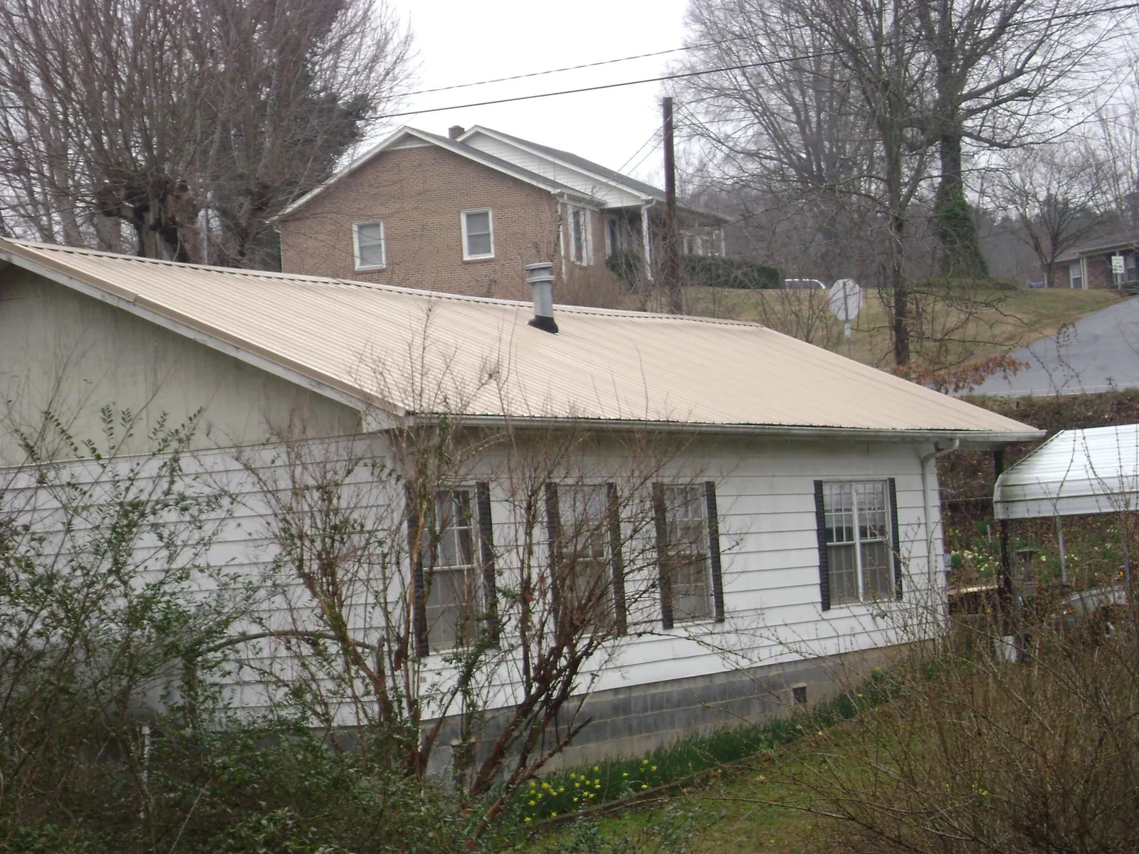 Tan metal roof on a white sided house set into a hillside — Commercial Roofing by Roofing Brothers in Kittanning